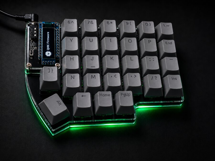Right half of a gray Lily58, with the QMK logo on screen and the coiled cable plugged in